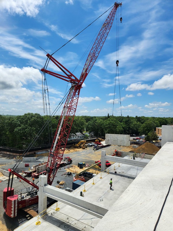 Rooftop view of a crane lifting a rectangular piece off of the ground.