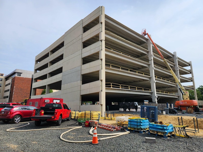 A ground view smaller crane pointed towards a parking garage structure. Trucks and supplies on the ground.