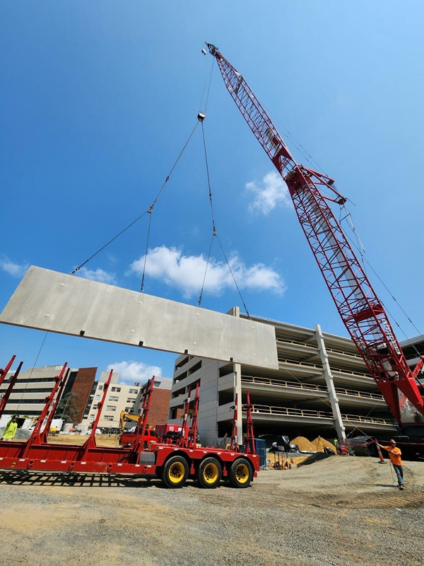 A red crane lifting up a rectangular piece towards a parking garage structure.