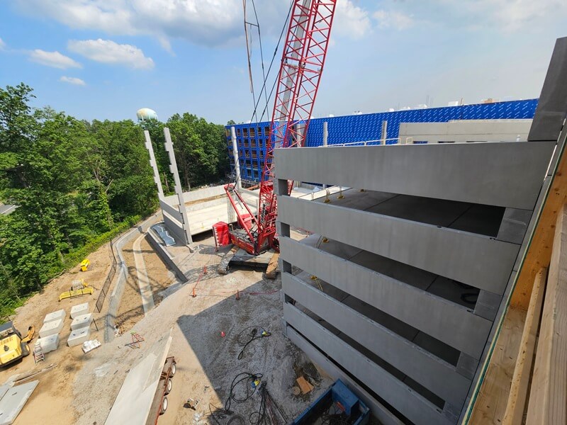 Parking Garage under construction. Red crane and treeline in background.