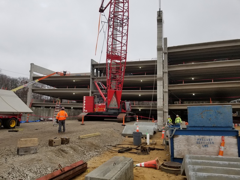 Parking garage construction site with various workers and equipment strewn about.