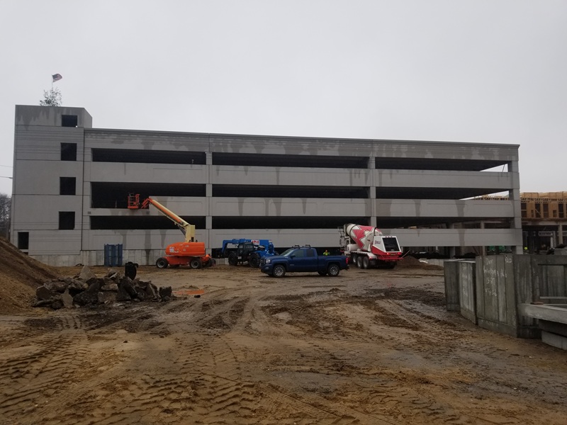 Parking garage under construction with various construction vehicles in front of it.